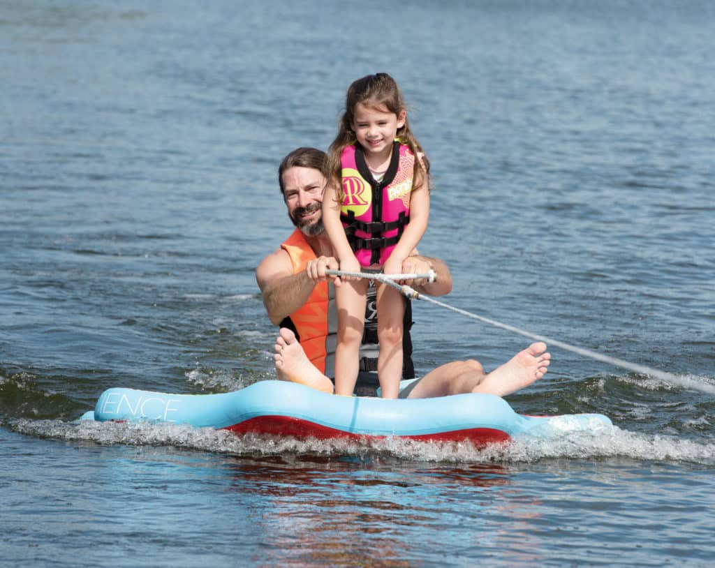 Child standing on inflatable disc pulled behind boat