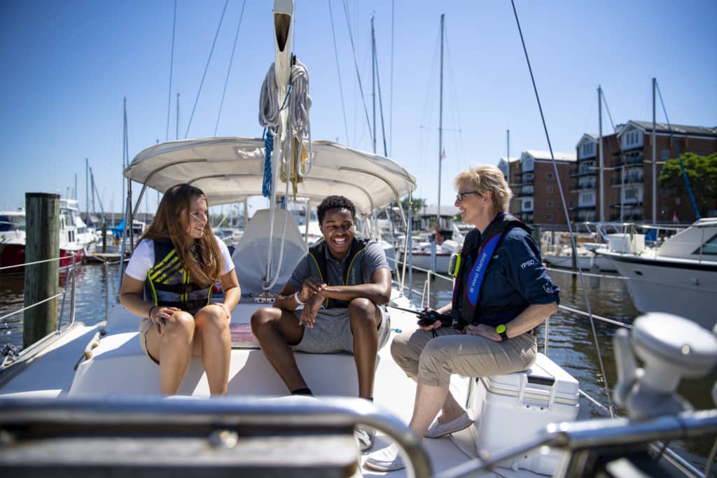 A group of boaters on a sailboat wearing life jackets